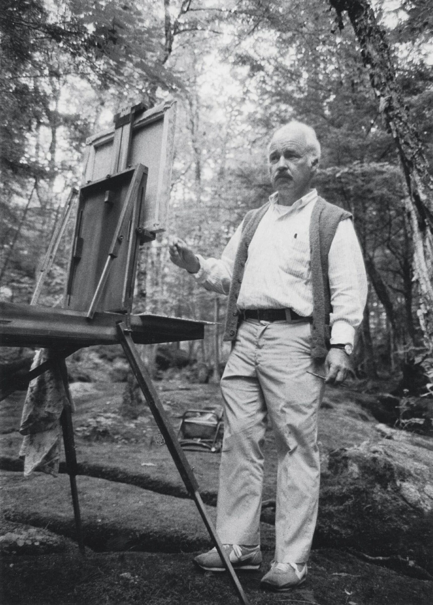 A black and white photo of an artist outdoors at an easel