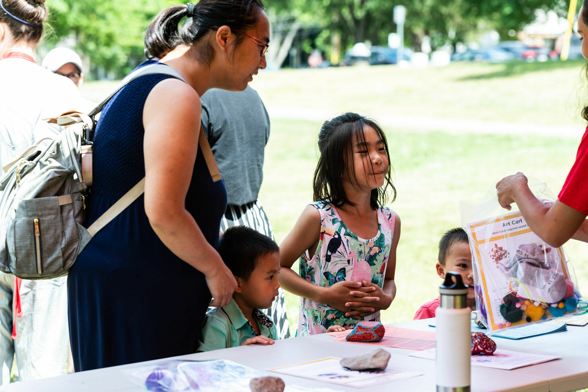 a family gathered around a table during the Art Cart event with a staff member or volunteer holding a free ArtKit with supplies