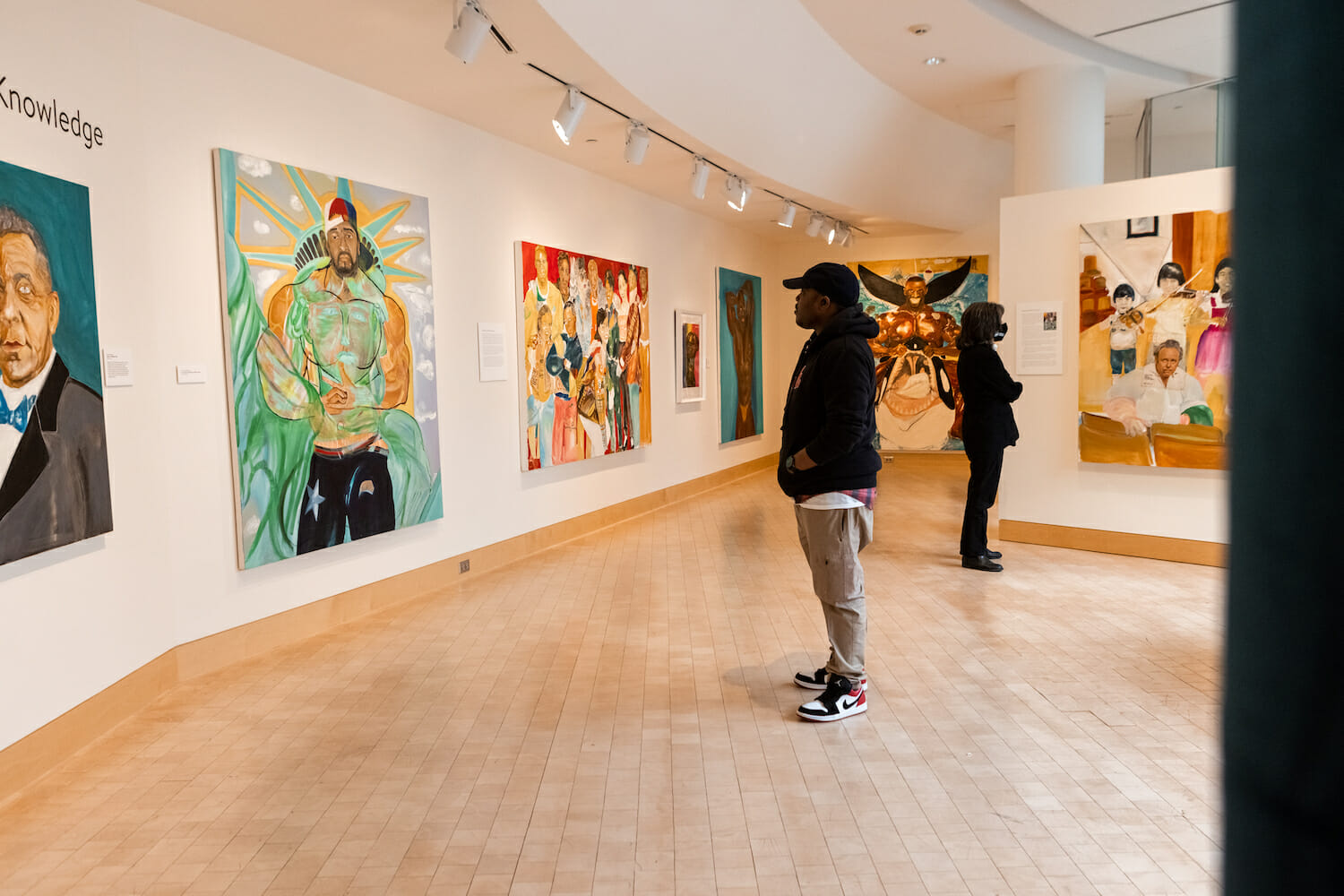 a person standing in the middle of an art gallery, looking at large paintings on the wall in a brightly lit space