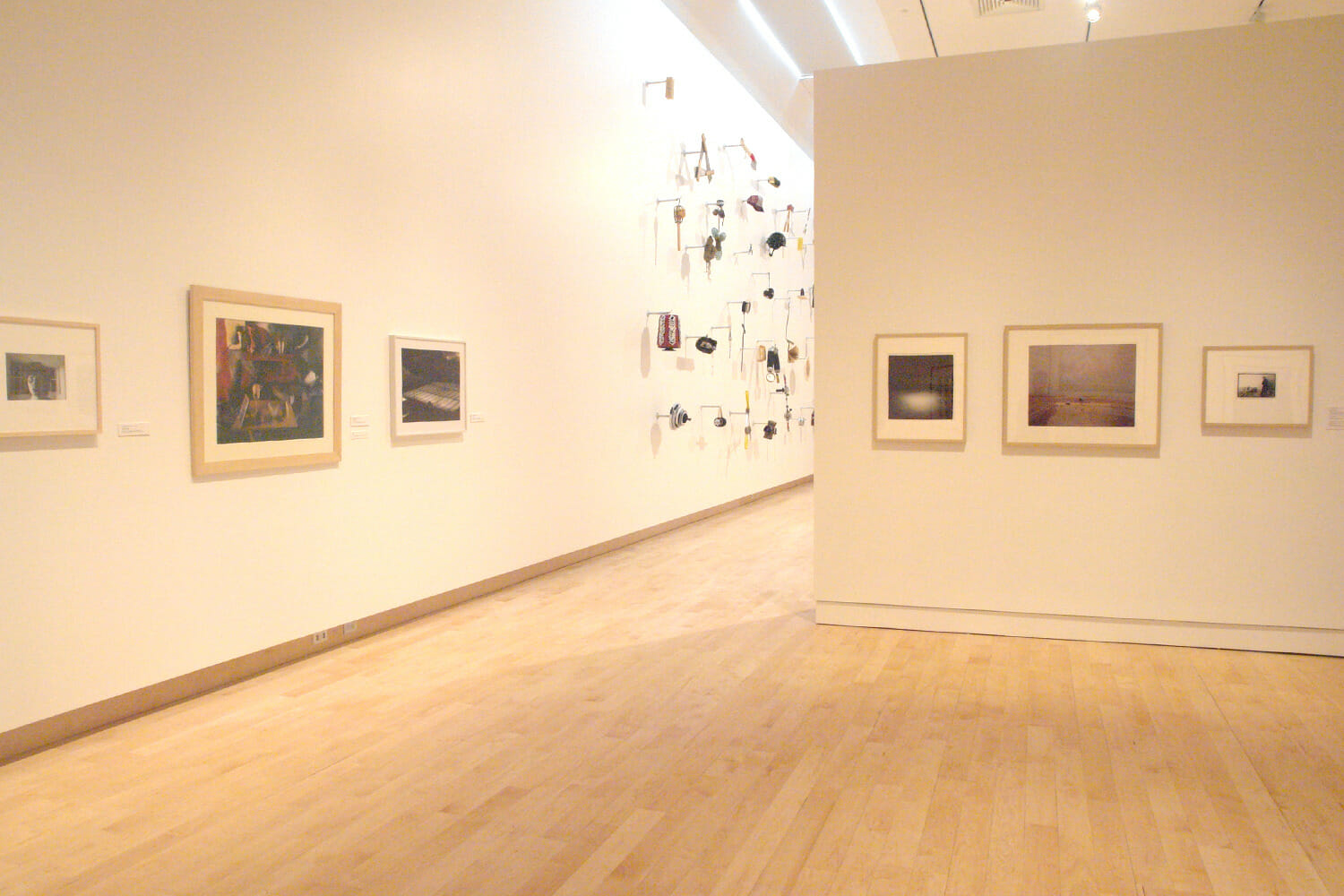 installation view of "In Depth," featuring six framed artworks hanging across two different walls and another artwork consisting of various objects attached to a wall