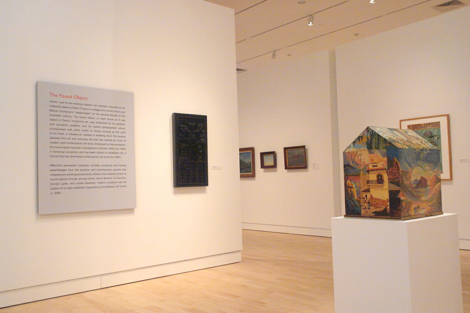 installation view of "In Depth," featuring artworks or photographs hanging on the wall with label text or displayed on a podium