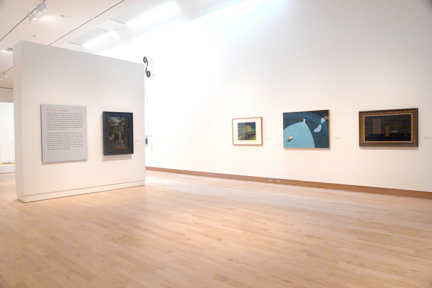 installation view of "In Depth," featuring at least four framed artworks hanging across different walls and exhibition text