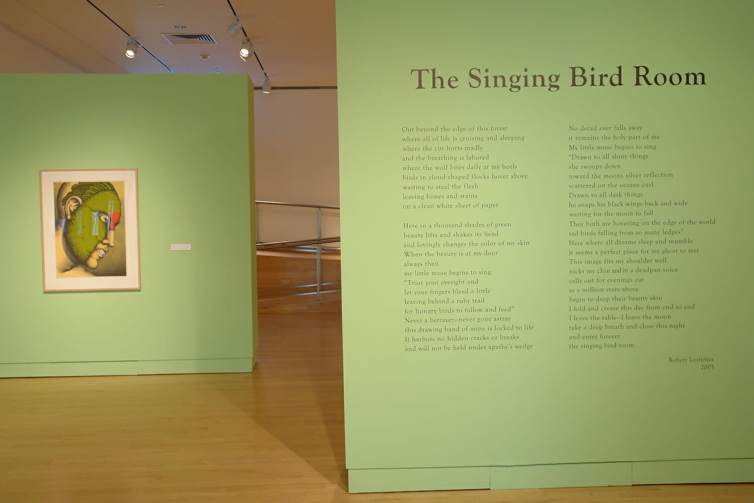 installation view of "The Singing Bird Rooms of Robert Lostutter" with a framed artwork hanging on a back wall and vinyl displaying text by Robert Lostutter