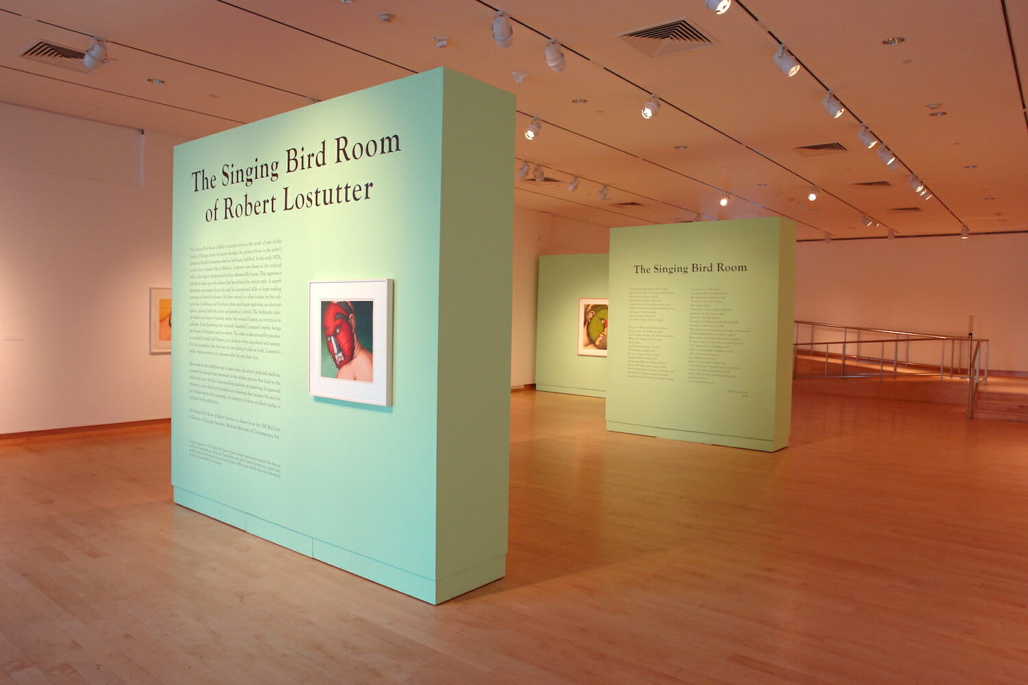 installation view of "The Singing Bird Rooms of Robert Lostutter" showing part of the title wall text, vinyl on the wall with additional text, and framed artworks hanging on walls