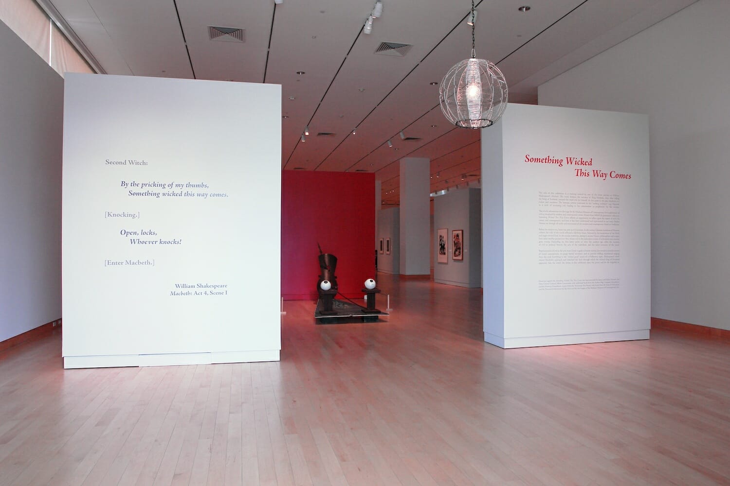 installation view of "Something Wicked This Way Comes" showing title wall text and a sculptural artwork in between