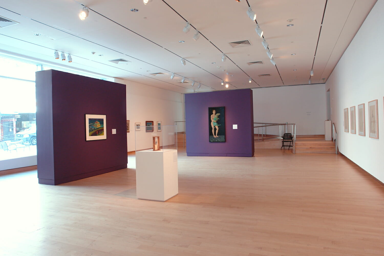 installation view of "the mystery beneath" showing framed artworks on the wall and a vitrine display case