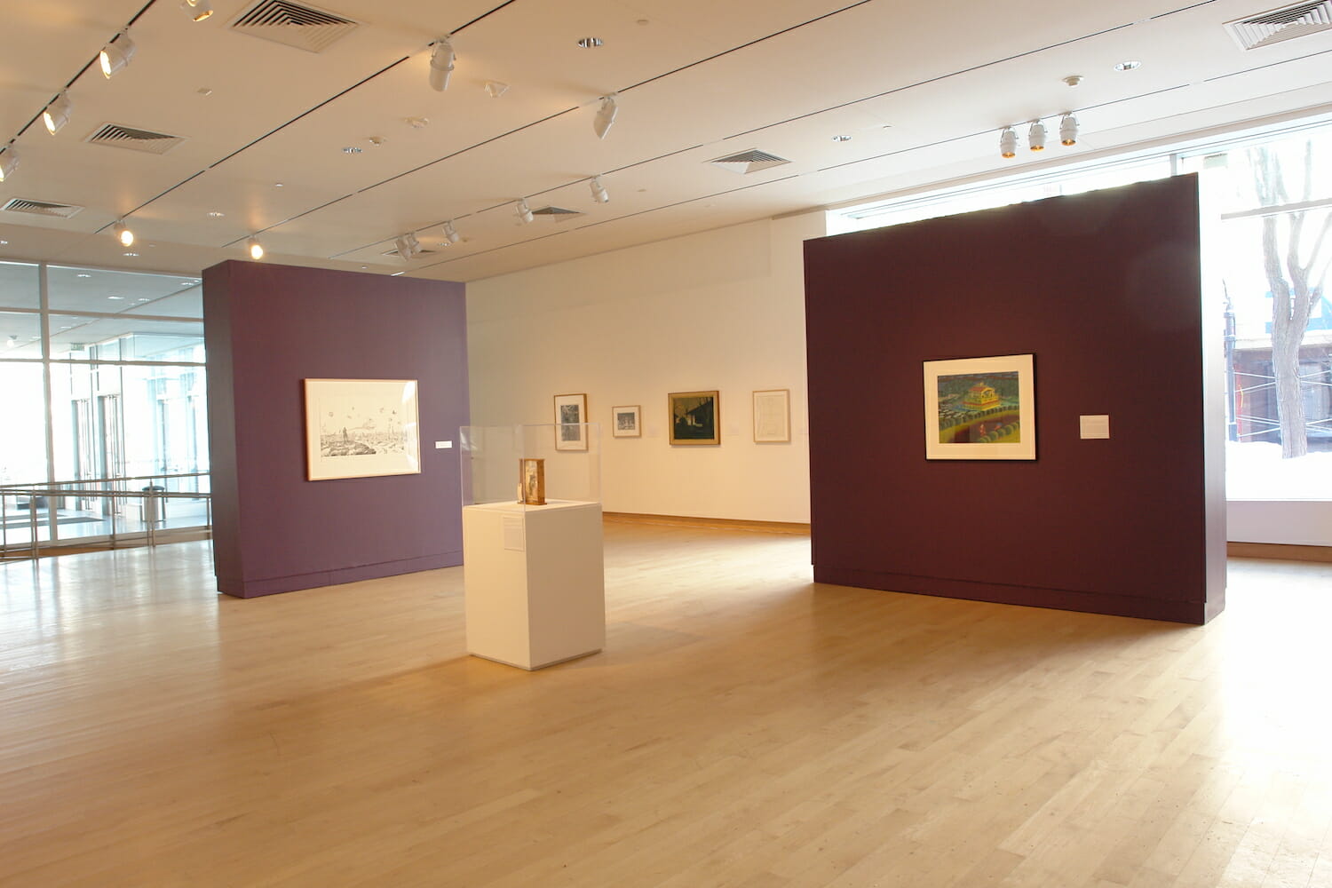 installation view of "the mystery beneath" showing framed artworks on the wall and a vitrine display case