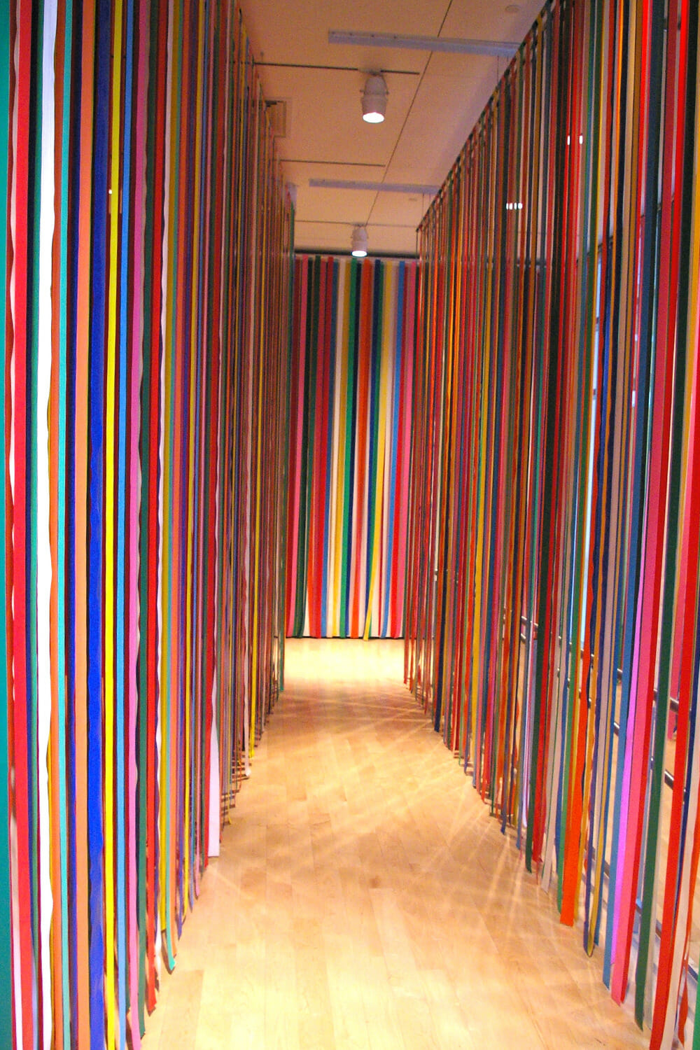 installation view featuring long colorful plastic ribbons hanging from ceiling and touching the floor
