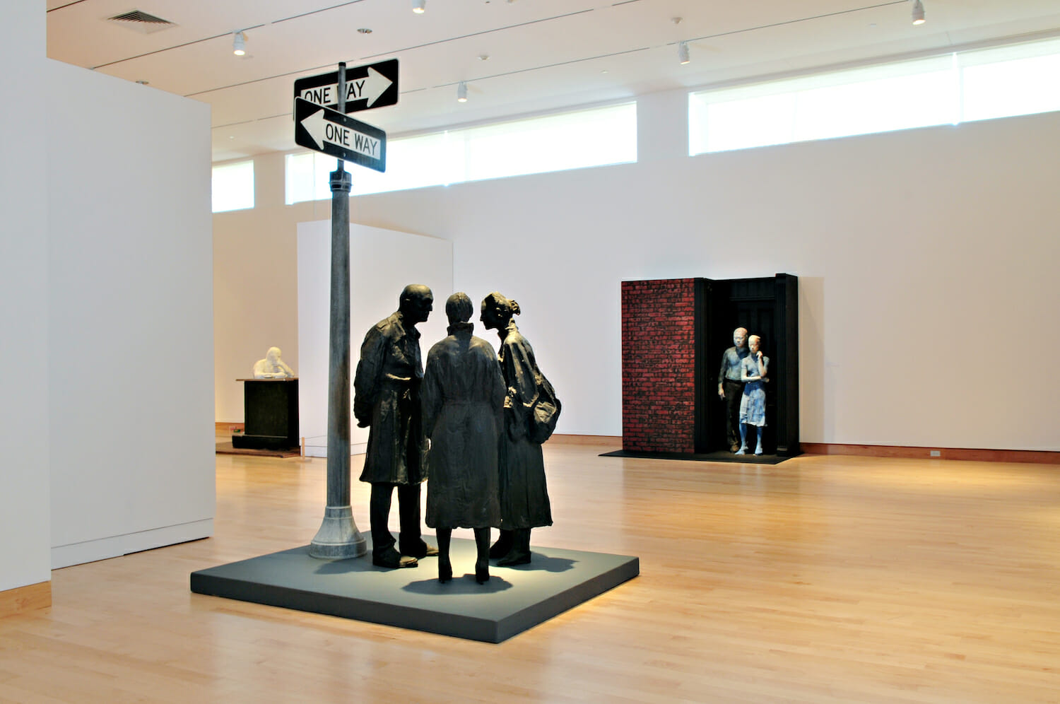 gallery installation view of George Segal: Street Scenes, featuring a variety of sculptures, including a sculpture of three people gathered under a street light