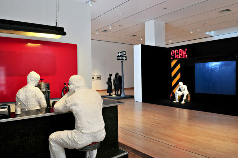 gallery installation view of George Segal: Street Scenes, featuring a variety of sculptures, including a sculpture of a person seated at a bar