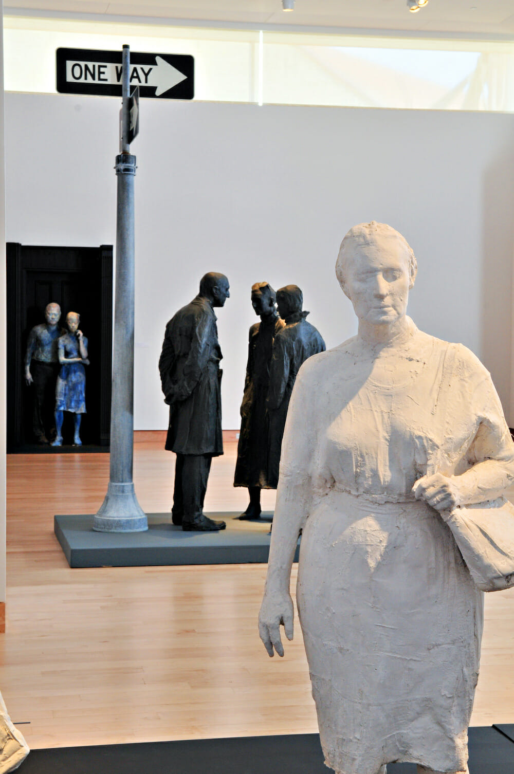 gallery installation view of George Segal: Street Scenes, featuring a variety of sculptures, including a woman wearing a dress and a shoulder or tote bag