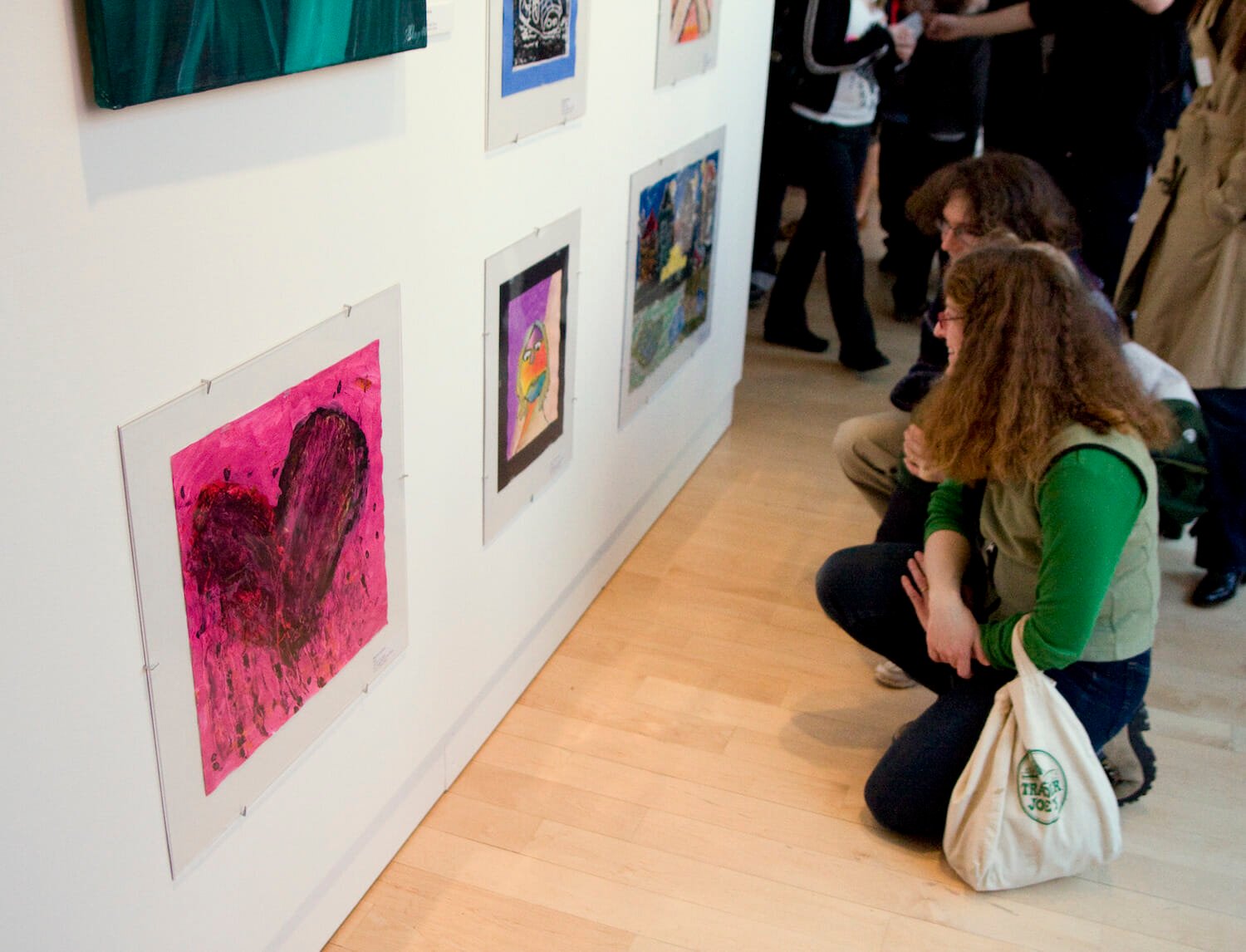 people kneeling or squating down to look at artwork made by children hanging on walls