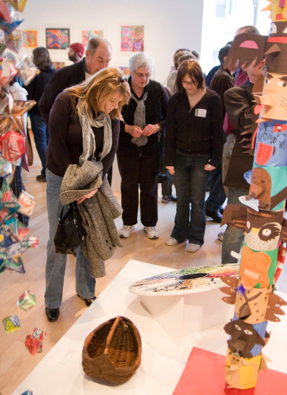 gallery visitors looking at sculptural works made by children on a low platform display