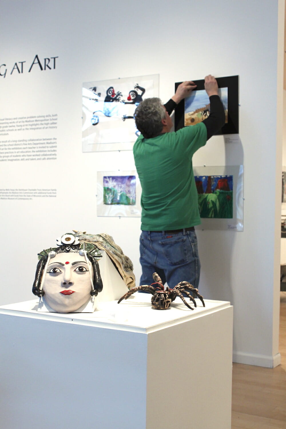 person hanging artwork made by a child on the wall, along with other artworks