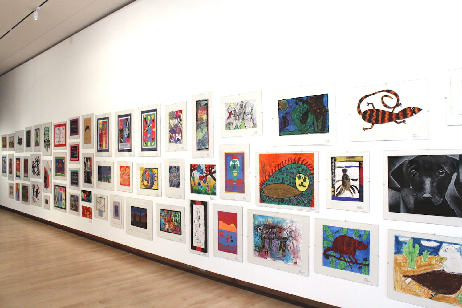 gallery installation view of Young at Art featuring rows of artworks on display across a wall