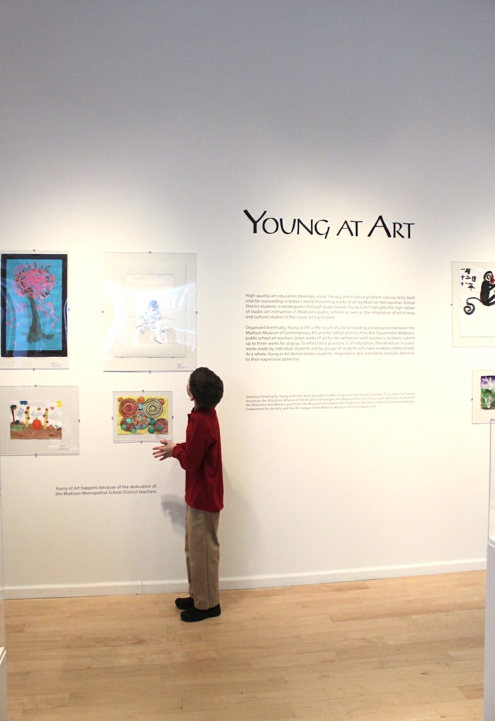child looking at artwork made by other children hung on a wall