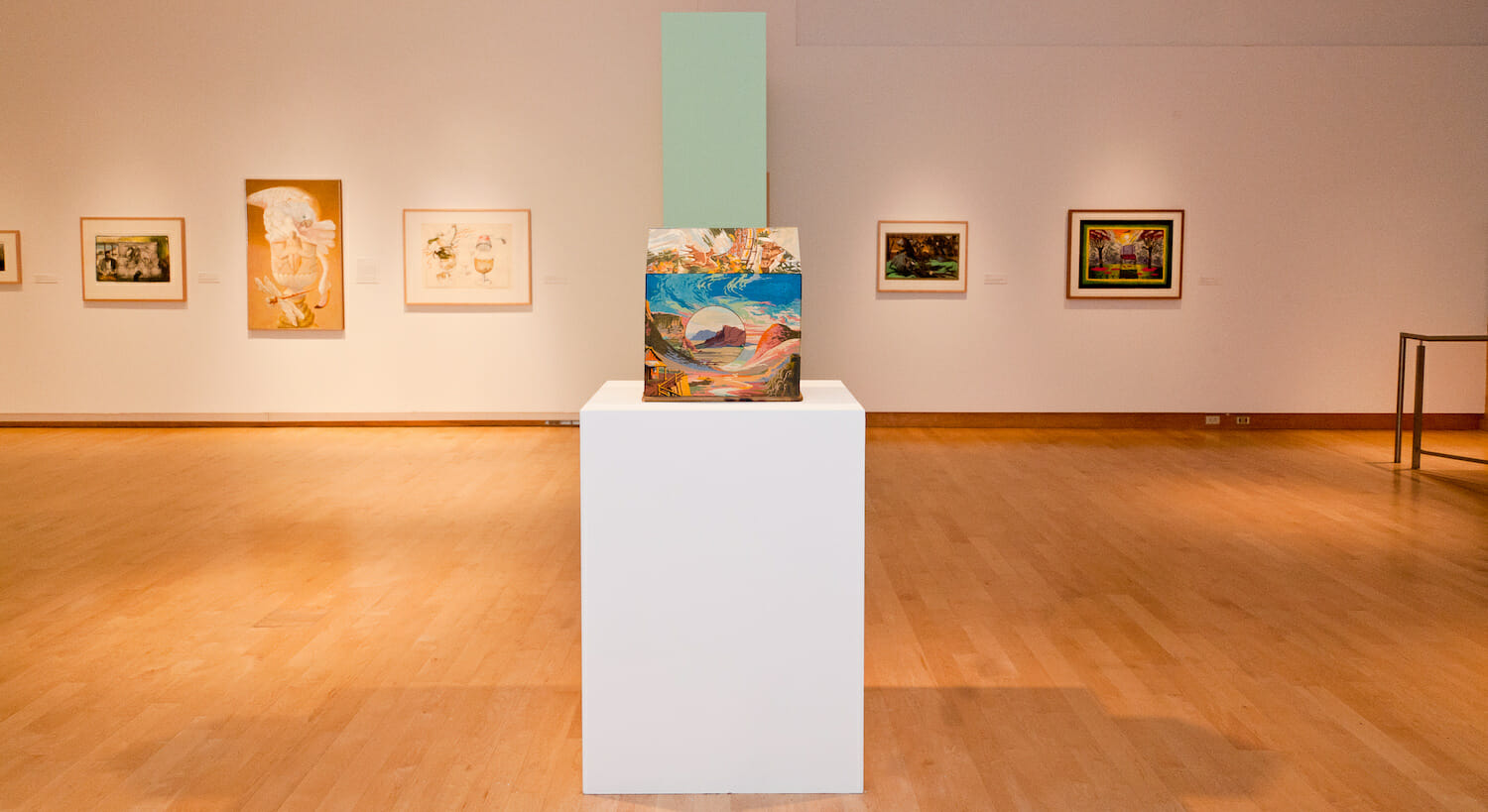 installation view of the exhibition Chicago School featuring a small house made of wood and canvas board on a tall display platform surrounded by artwork hanging vertically across walls