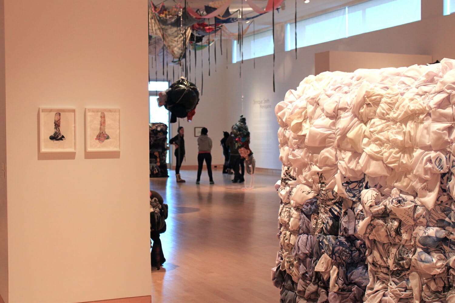 installation view of Shinique Smith: Menagerie featuring an abstract sculpture at the forefront of the photo, and a group of visitors and additional abstract sculptures in the distance