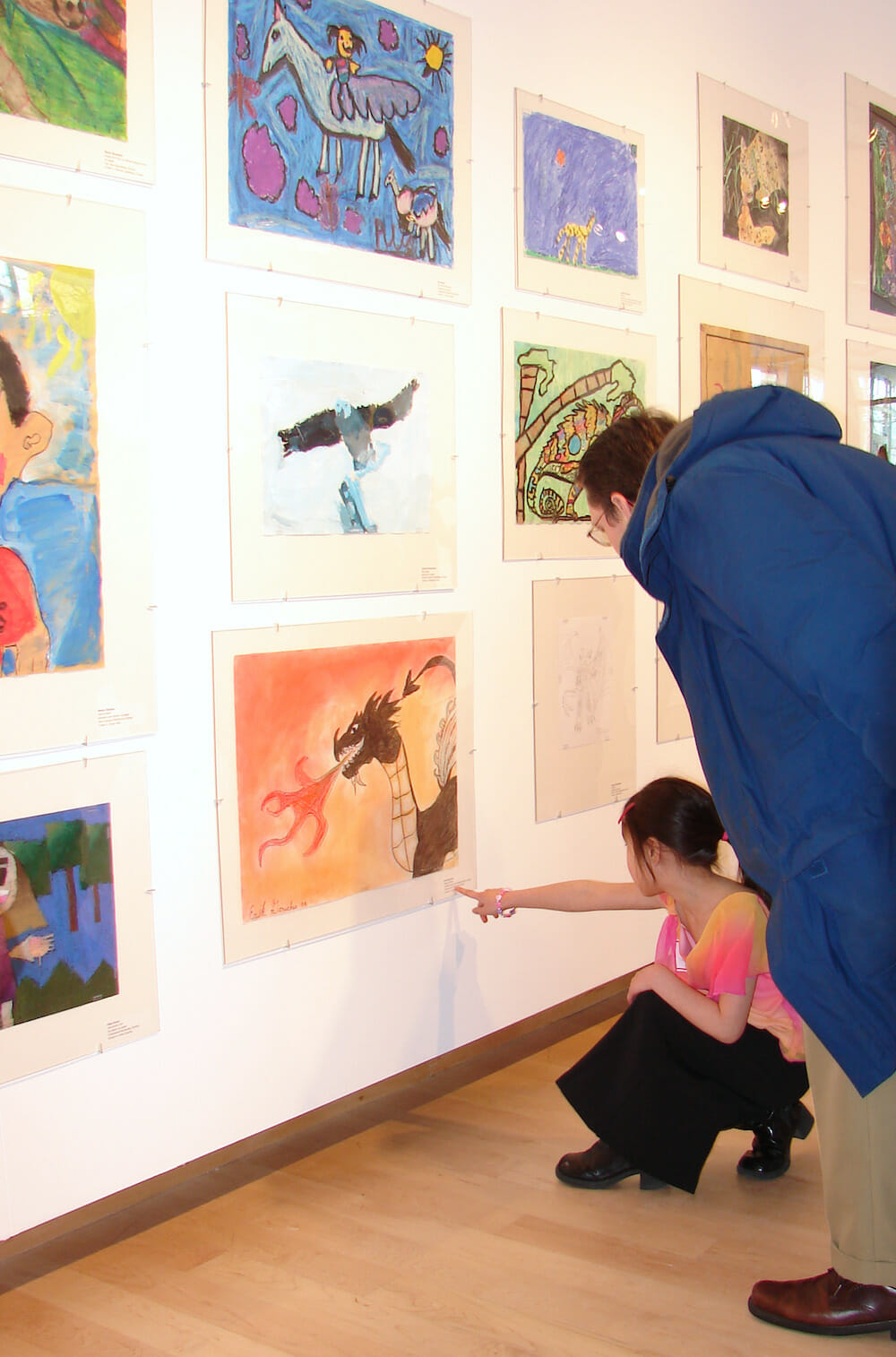 a child and an adult looking closely at artworks made by children on walls