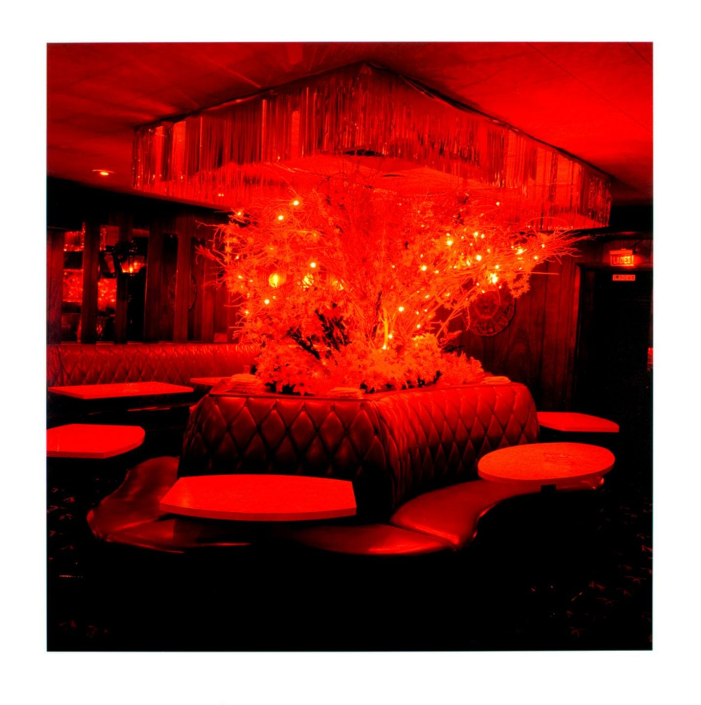 photograph of a darker room, partially lit by an elaborate arrangement of lights in the center, surrounded by leather couches with smaller tables in front of each segment