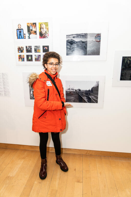 Child artist posing for the camera while standing in front of their artwork.