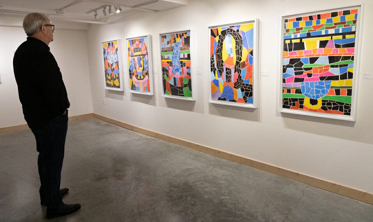 A person standing in front of five large art canvases hanging on a gallery wall.