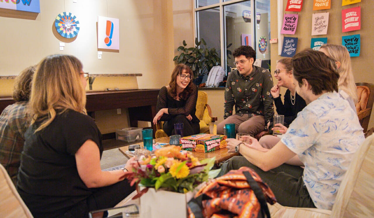 A group of people seated on couches and conversing or laughing with each other during Gallery Night.