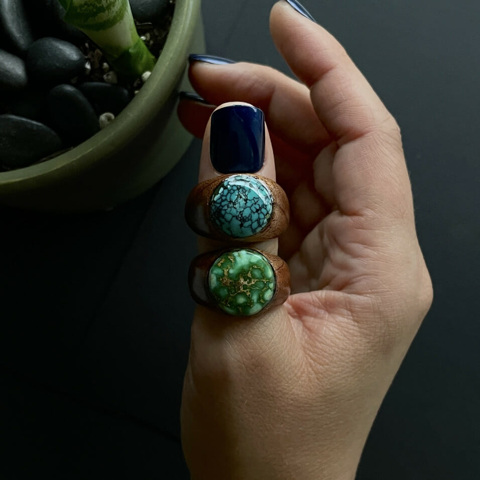 A hand with two wooden rings and inlayed turquoise on a thumb.