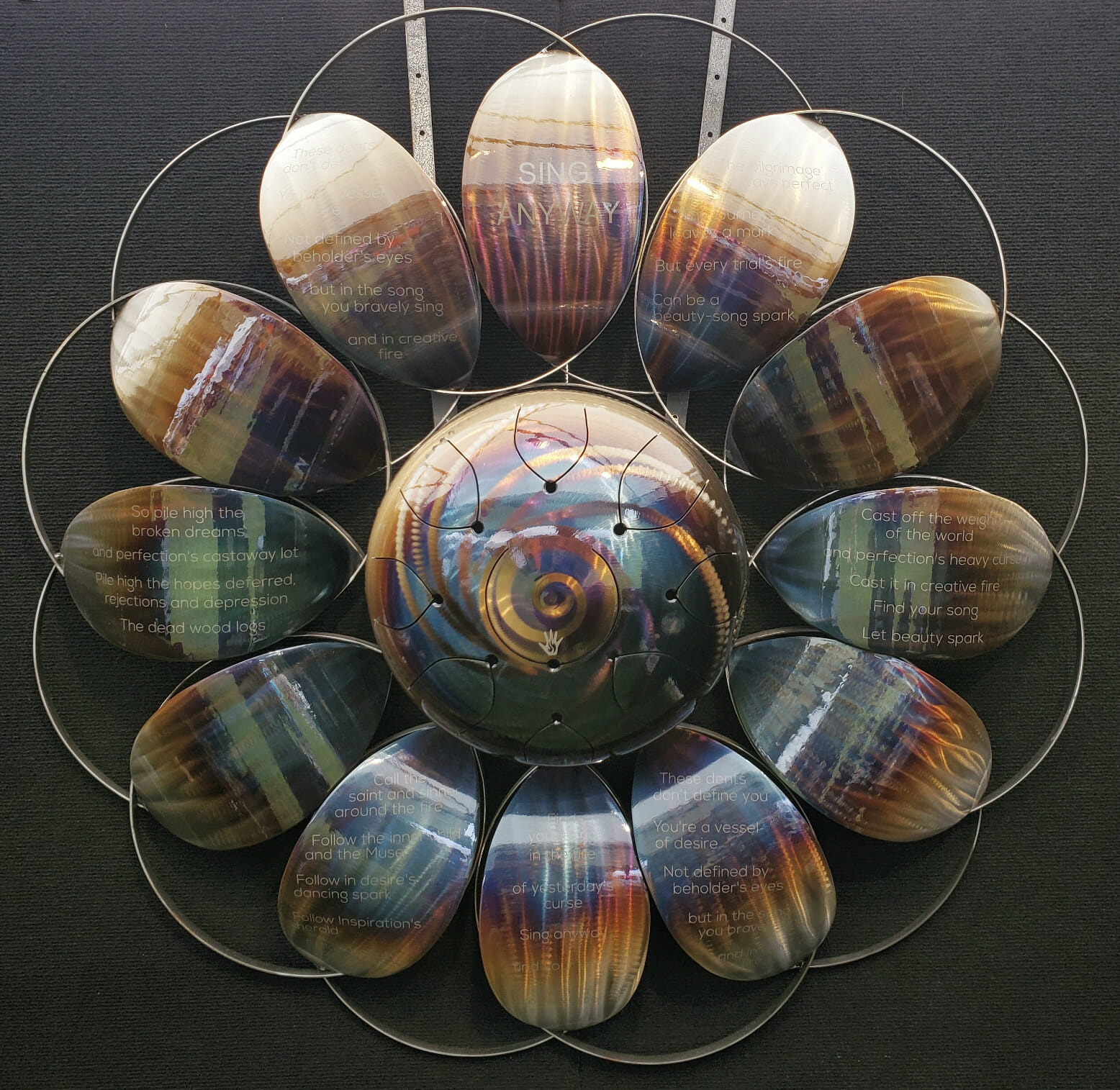 Metal artwork in a flower-like shape, with etched lines from a poem.