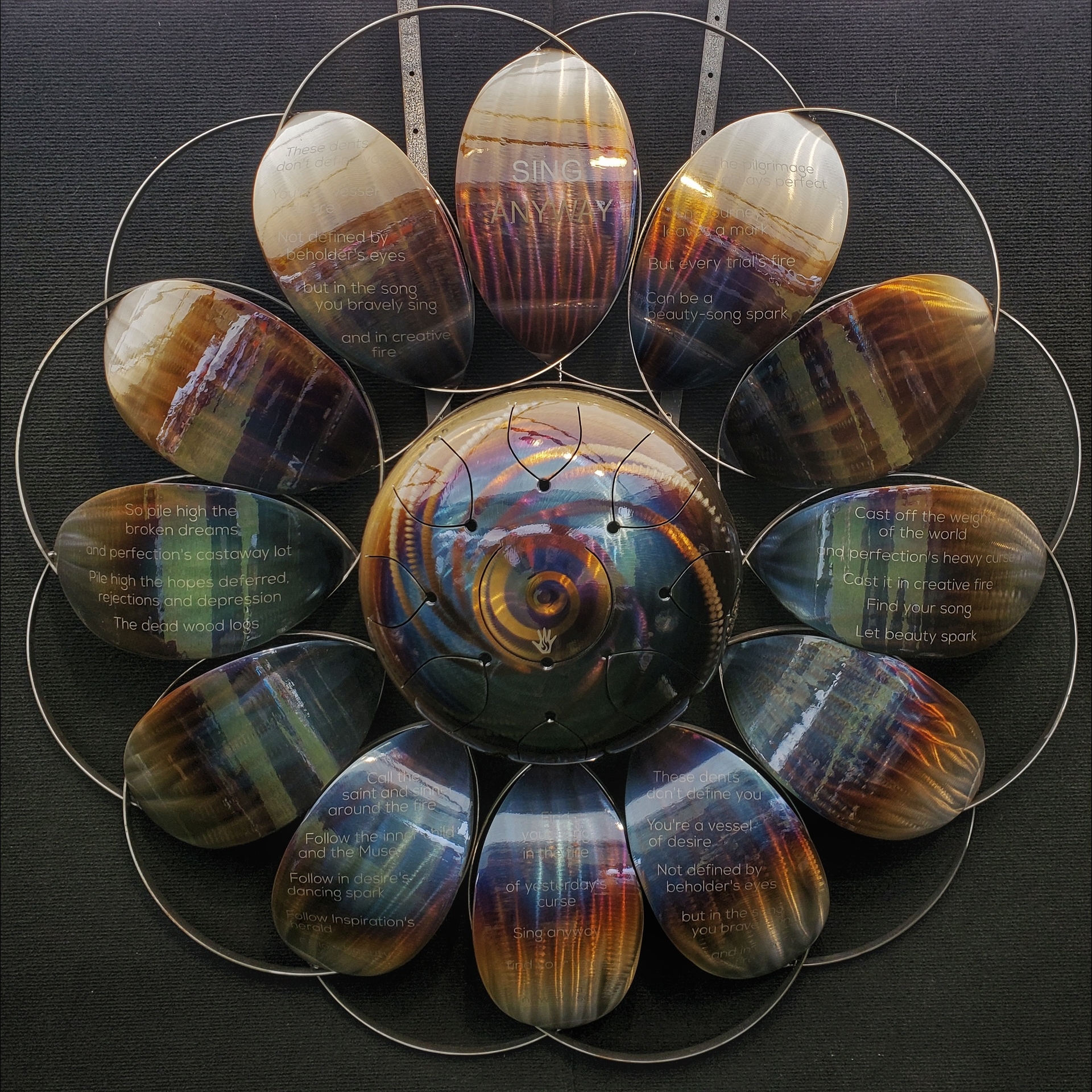 Metal artwork in a flower-like shape, with etched lines from a poem.