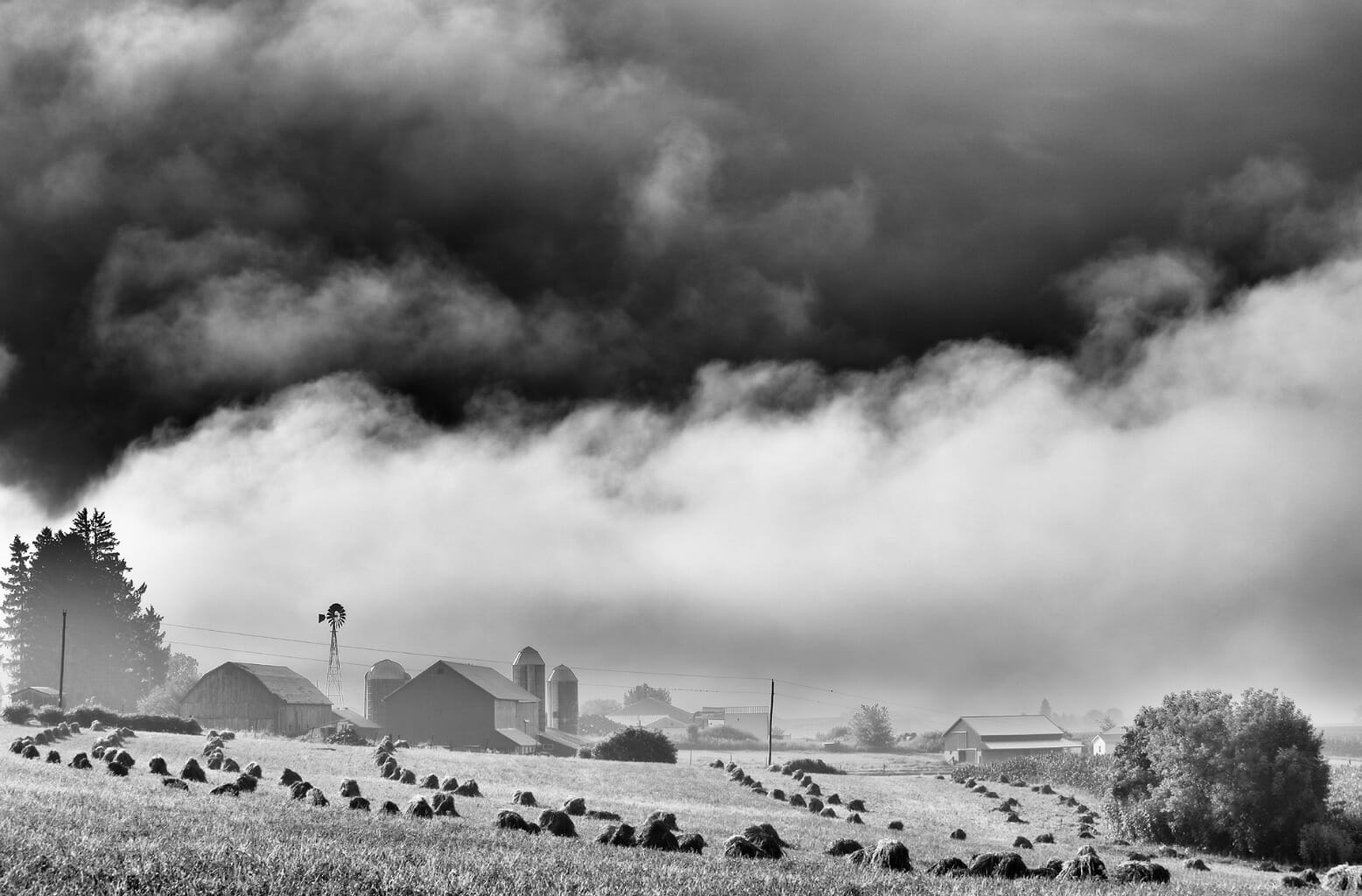 Landscape photo with various buildings in the distance, clouds, and wheatstacks.