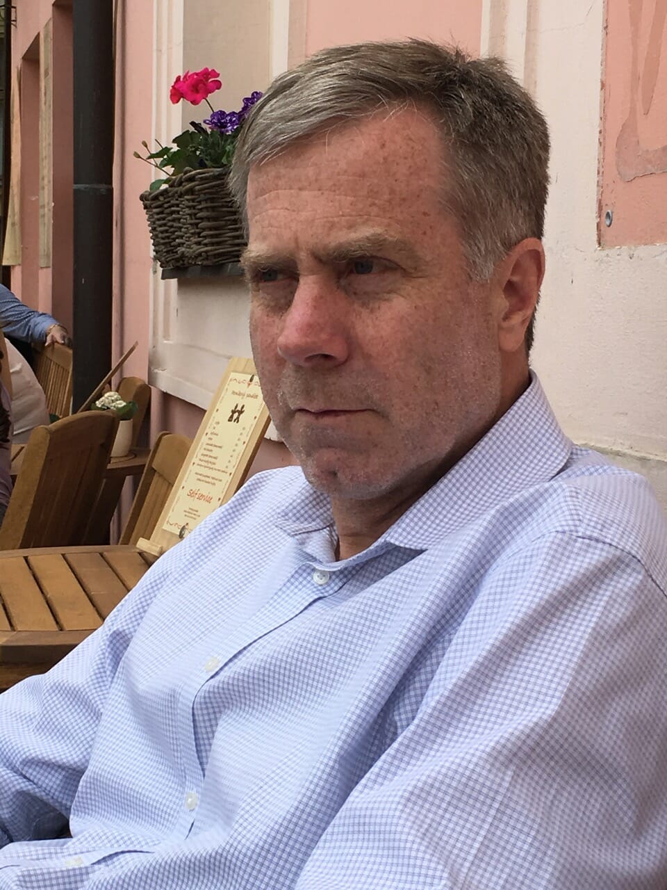 Bruce, wearing a blue shirt, seated outdoors in front of a pink wall.