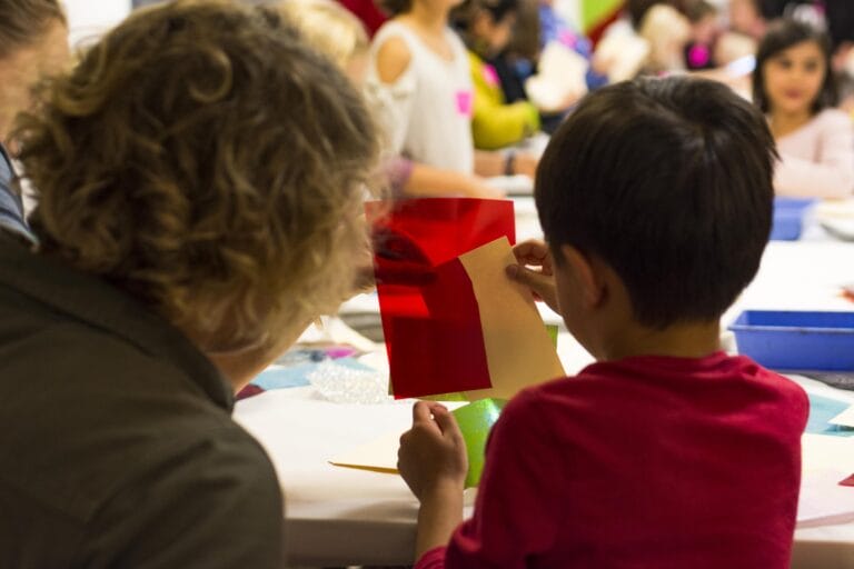 A child wearing a red shir and an adult work on an art activity with translucent red material.