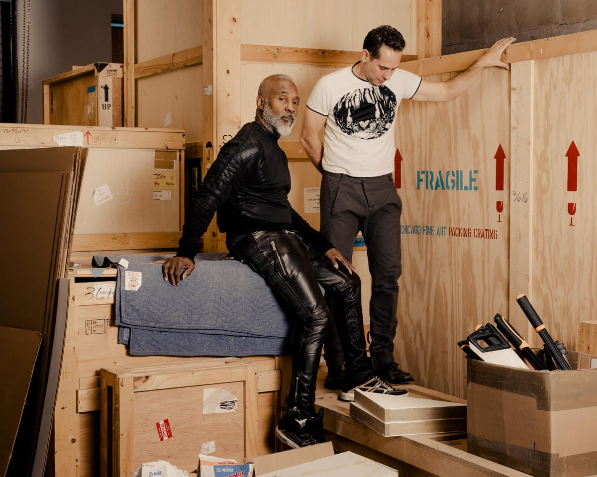 Artists Nick Cave and Bob Faust standing on wooden crates.