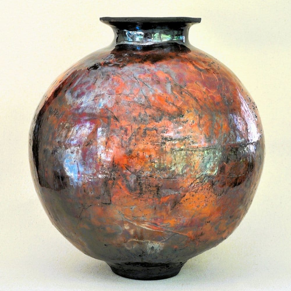 A spherical raku ceramic vessel with oranges and greens.