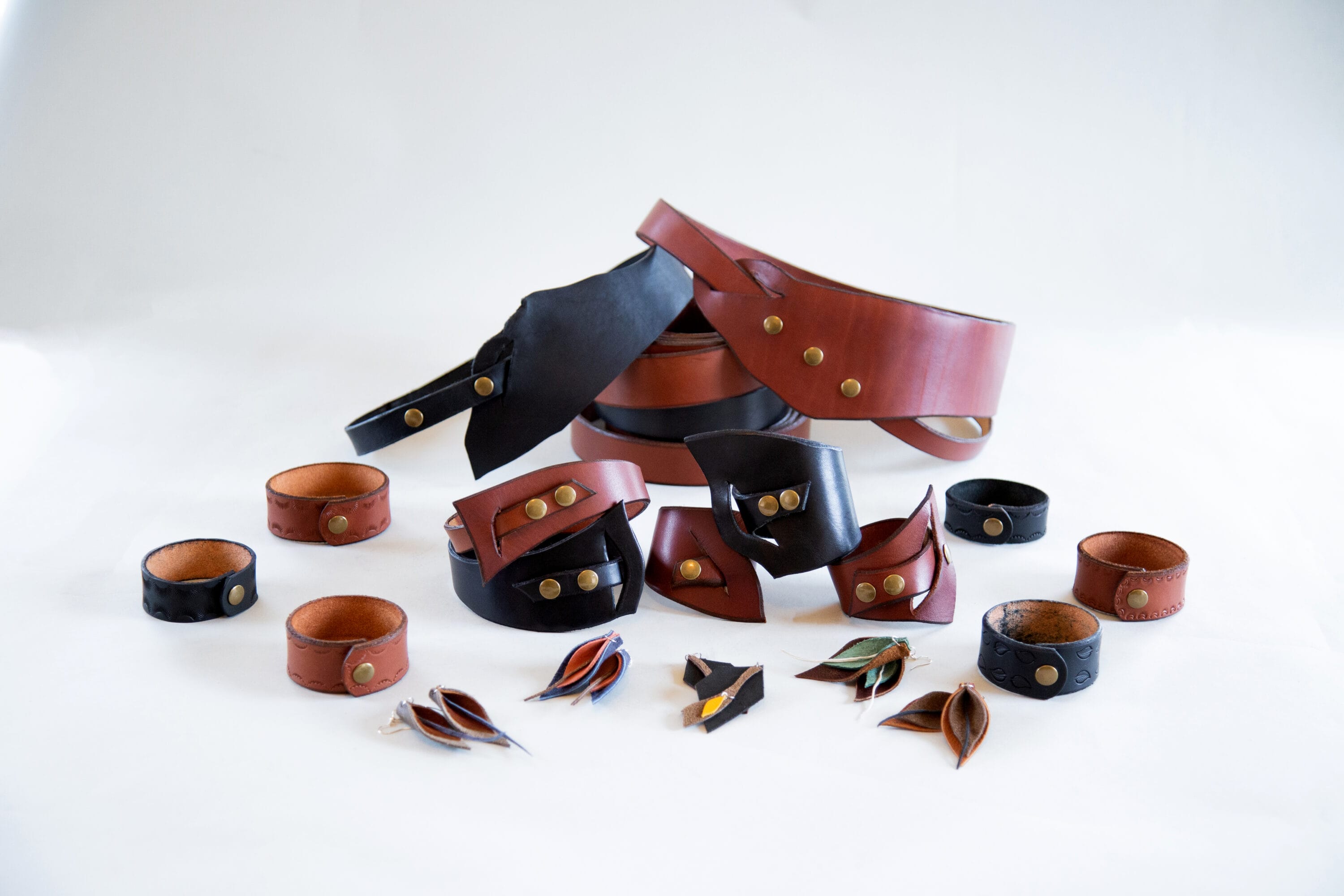 An array of leather wrist bands, belts and other wears on a white photo set up.