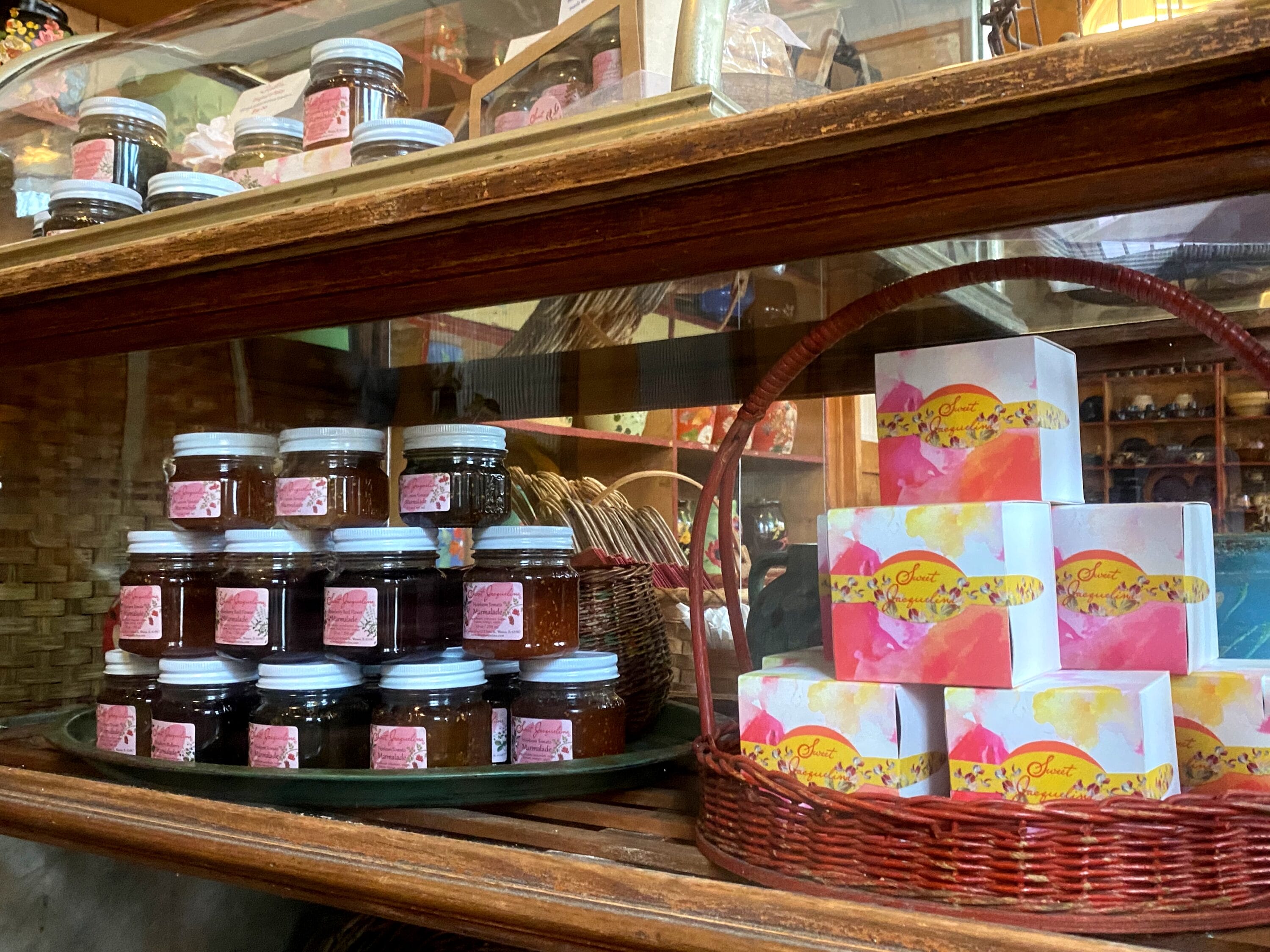 Several honey colored jam jars stacked next to similarly stacked colorful boxes in a basket.
