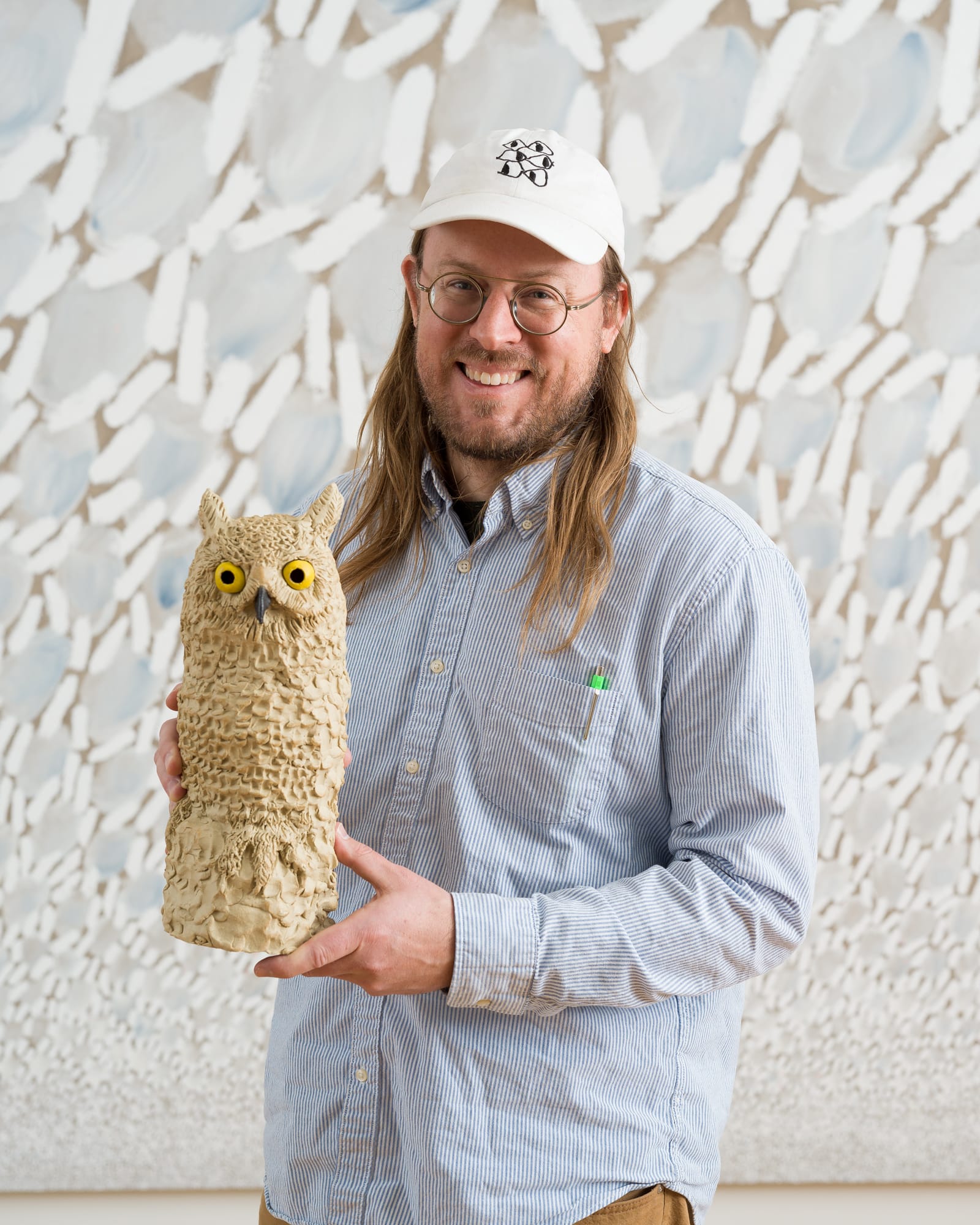 A man with long hair and a hat holding an owl sculpture.