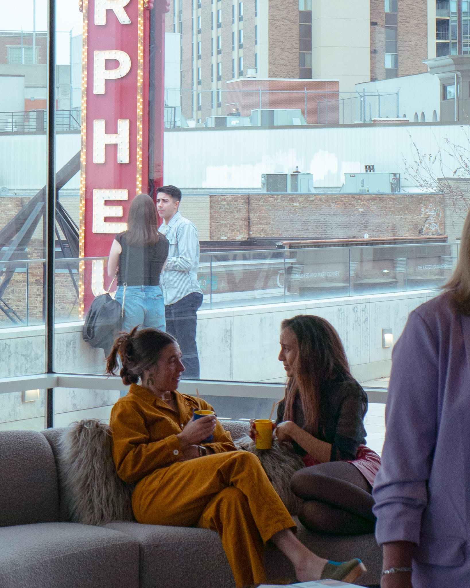 People talking on a couch with other people behind them.