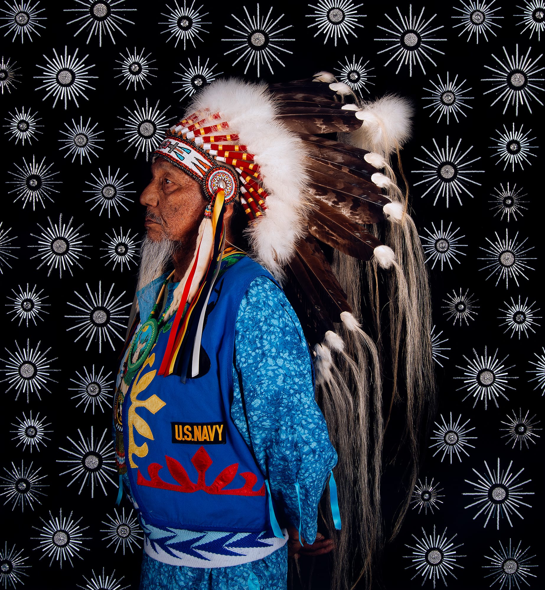 A man in an indigenous headdress with a U.S. Navy vest on.