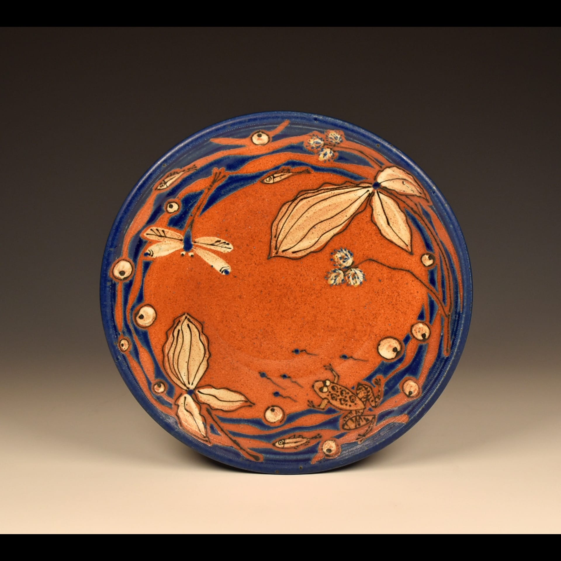 An orange plate with blue dragon fly designs painted on it.