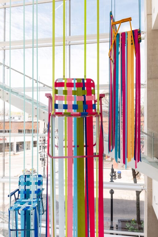 Colorful chairs with ribbons on them hanging in a stairwell.