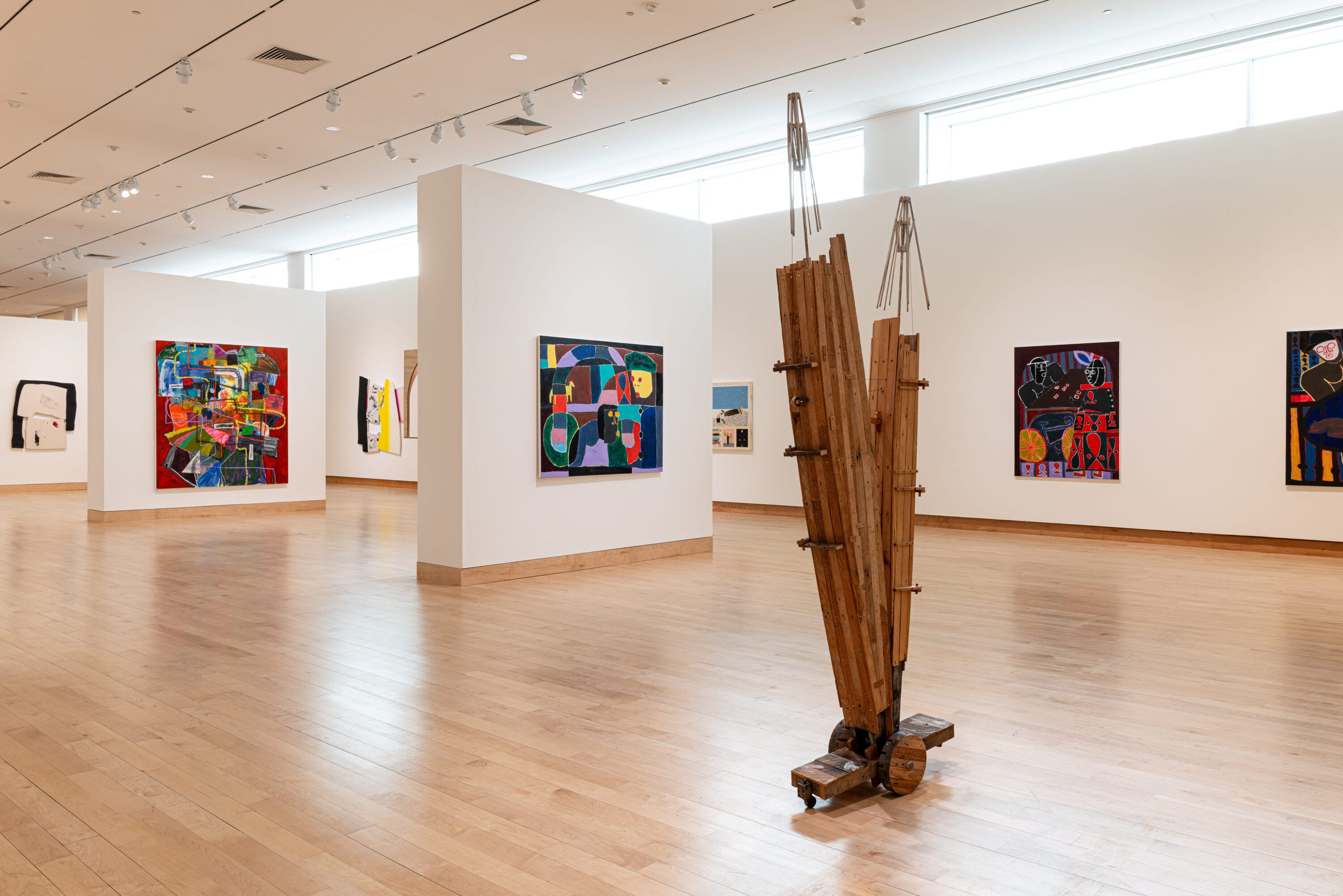 A gallery space with art work on the wall and wood sculpture.