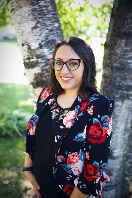 A woman in a floral shirt smiling in front of a tree.