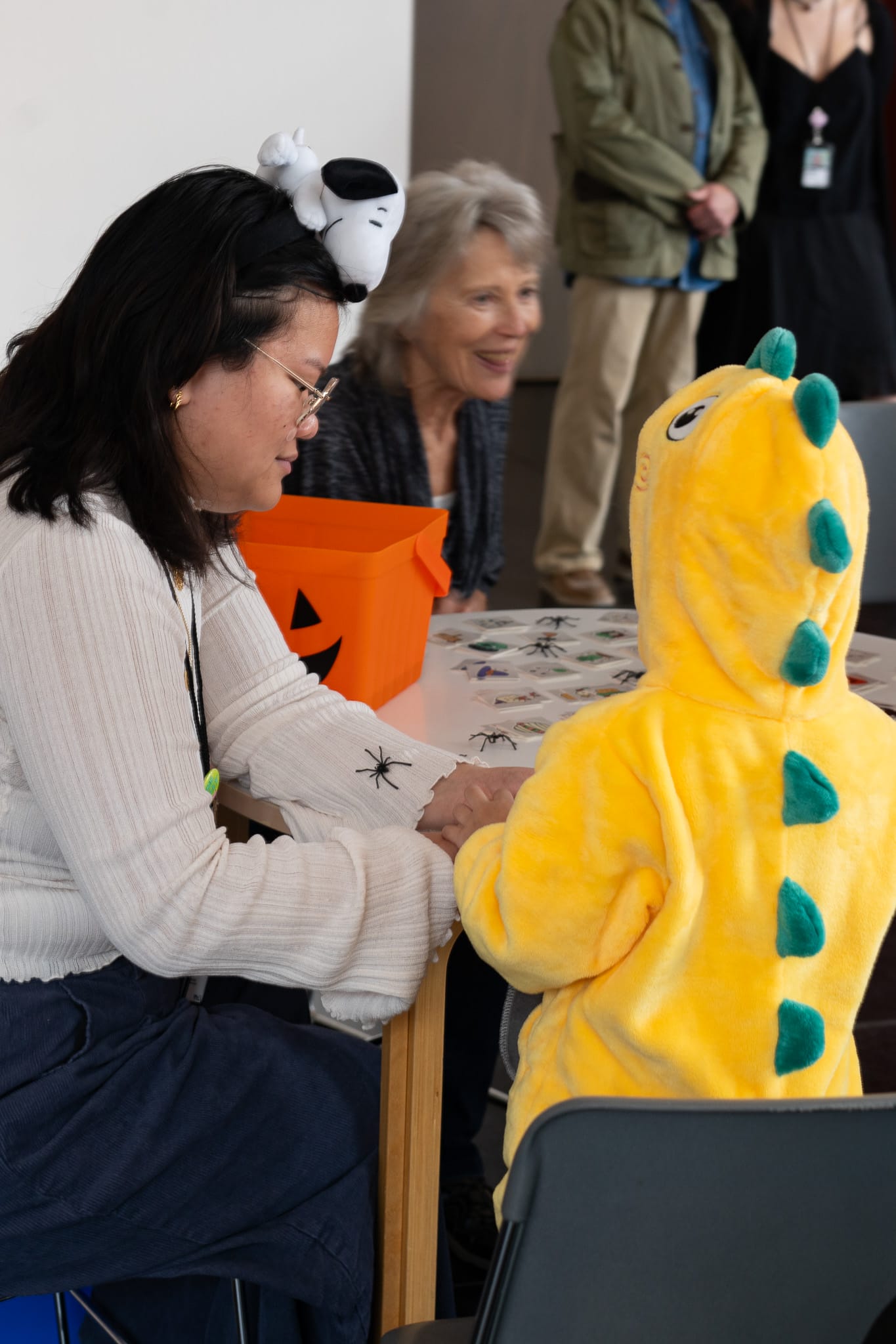 A child dressed as dinosaur drawing something with the help of an adult.