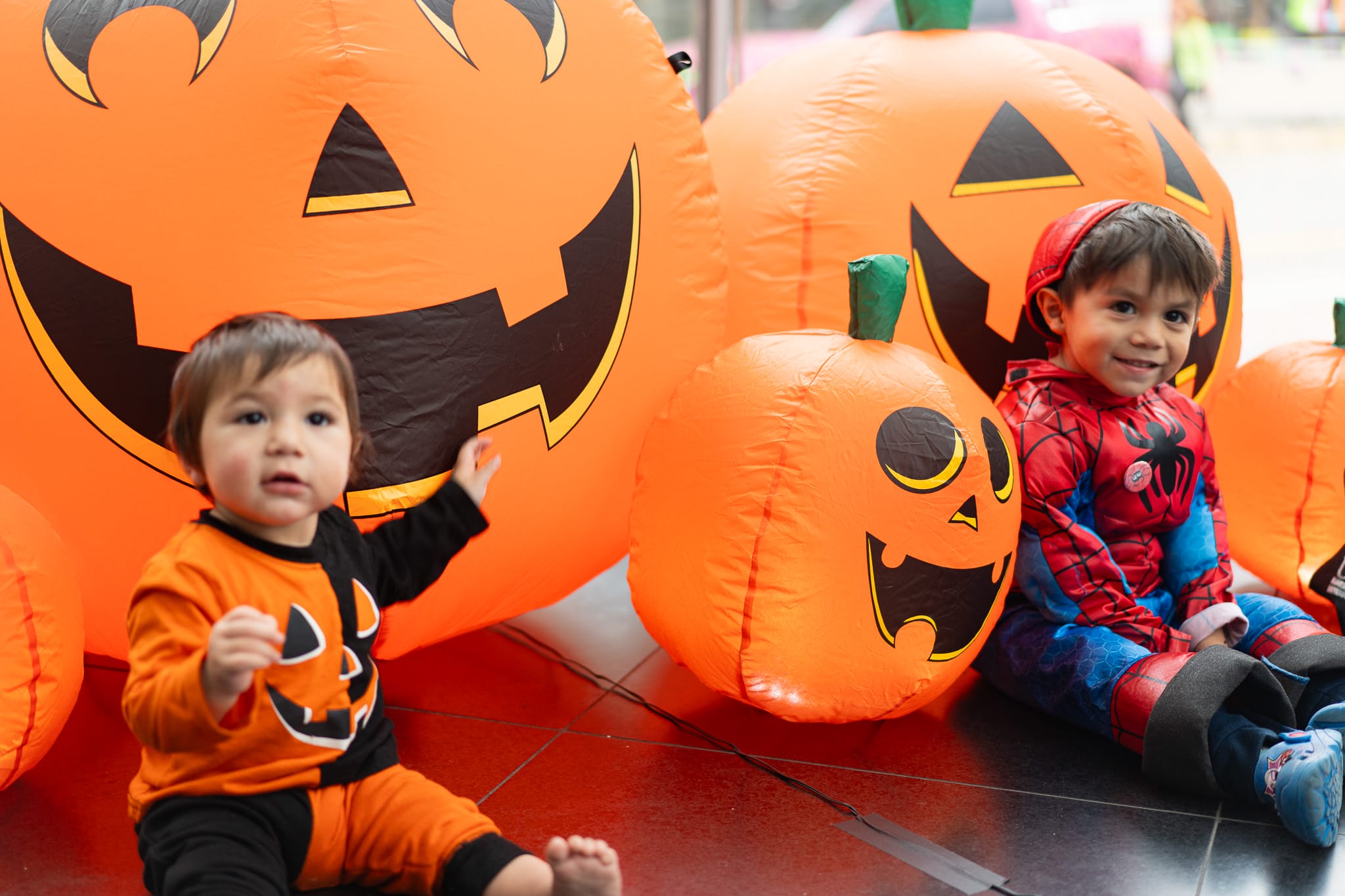 Two kids by pumpkins dressed in Halloween costumes.