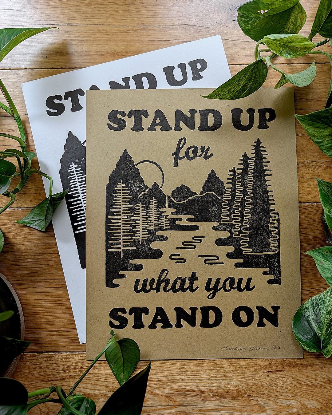 Graphic art prints on a table surrounded by plants.