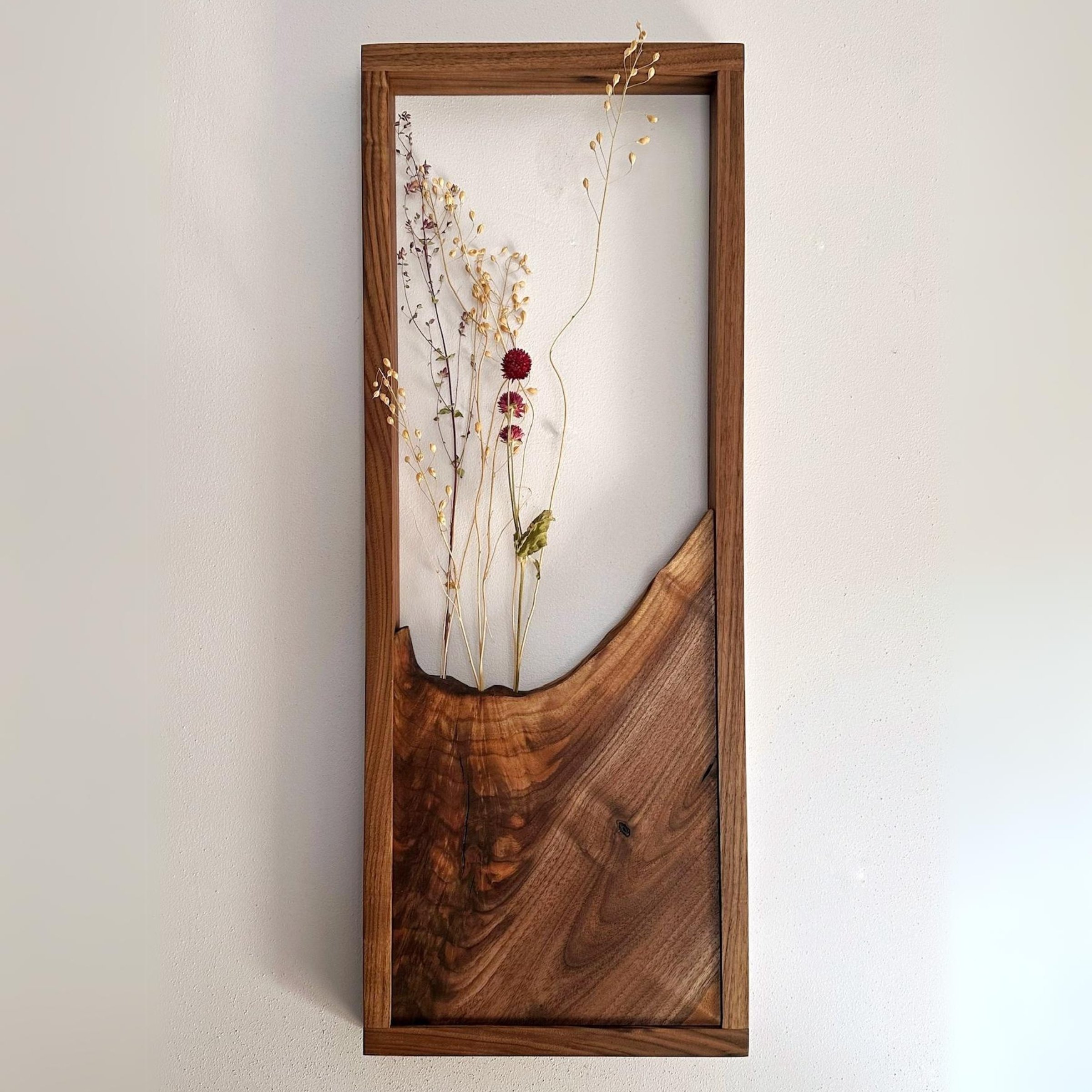 A wooden frame with dried flowers hanging on a wall. 