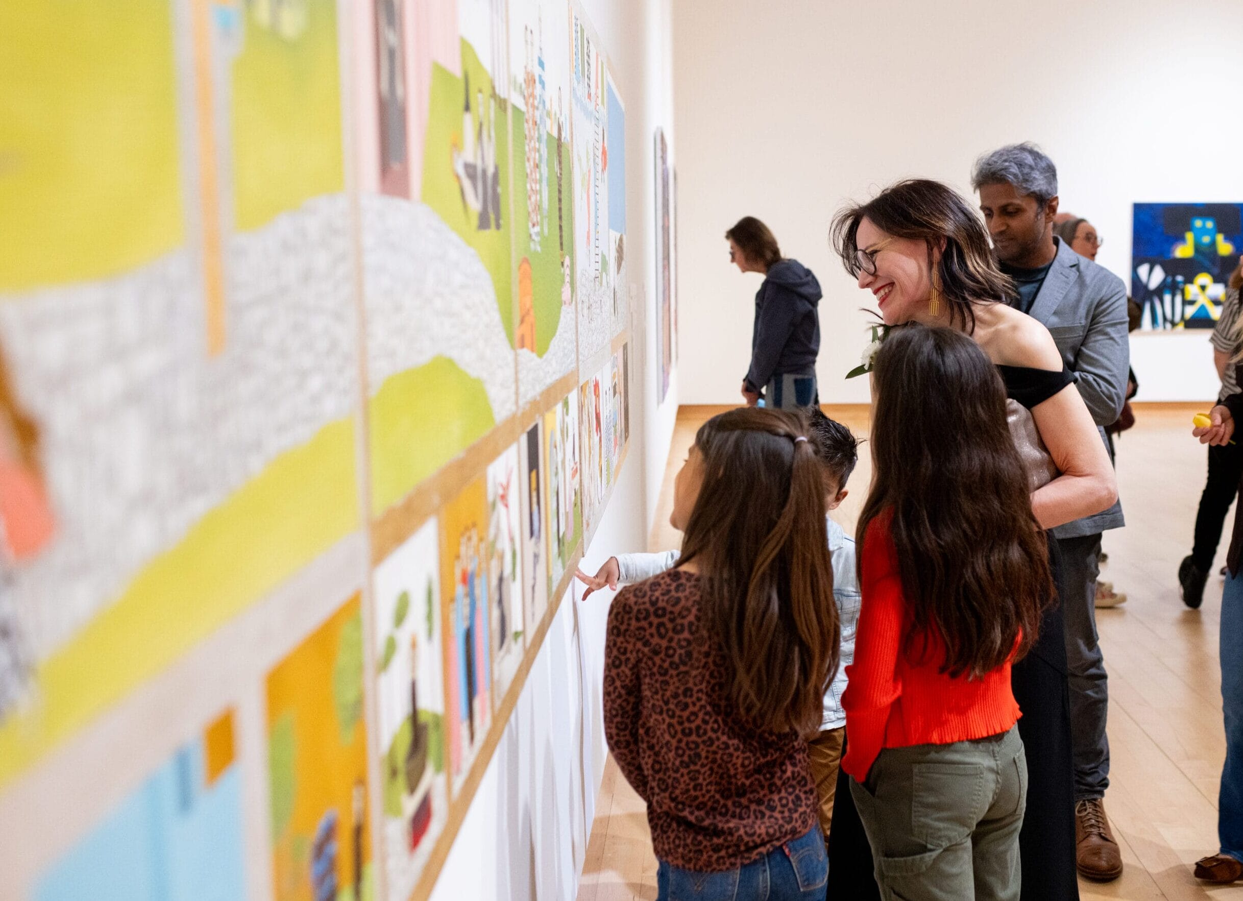 A group of people smiling while looking at a painting hanging on the wall.