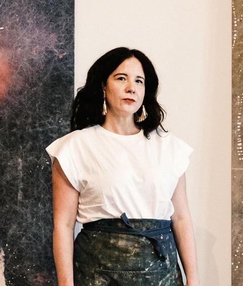 A woman standing wearing a white shirt and hoop earrings.
